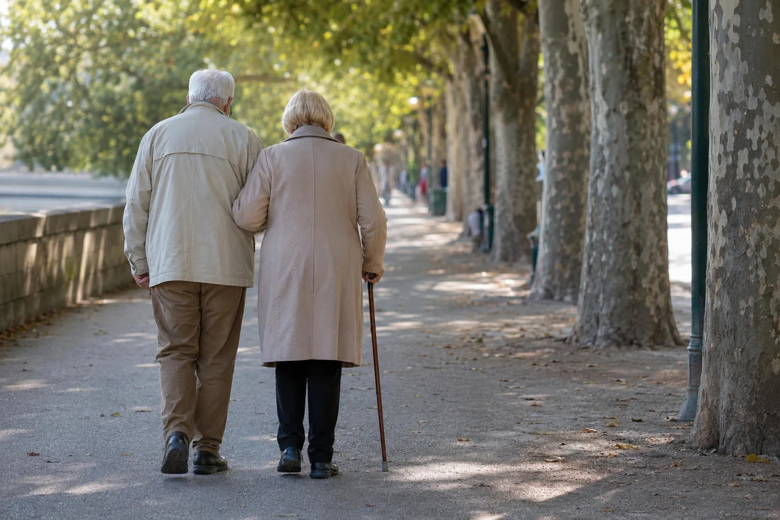 Un couple âgé marche bras dessus bras dessous sur une allée arborée, la femme s'aidant d'une canne